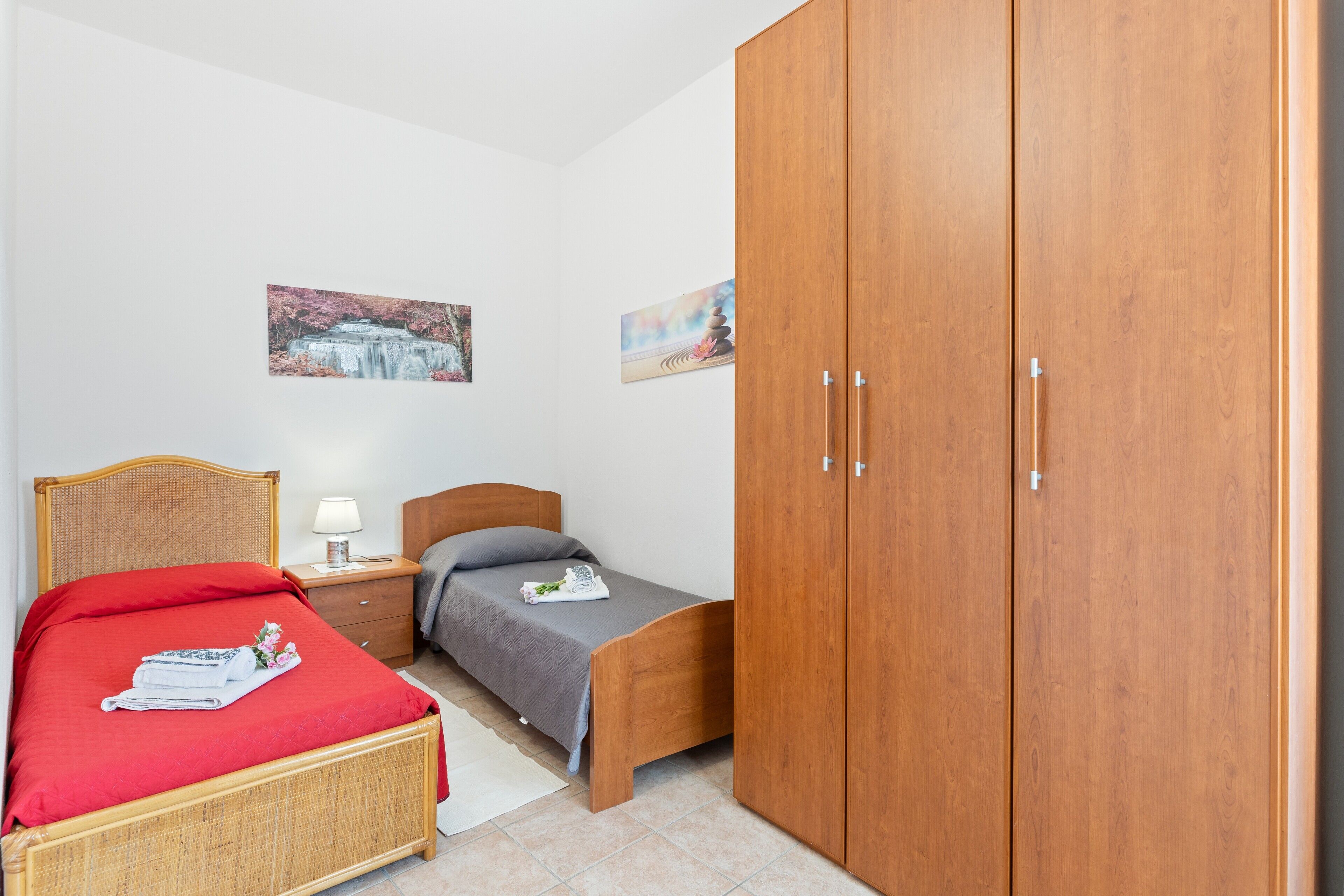 A bedroom with a bed, a wooden wardrobe, a nightstand, and two wall-mounted paintings.