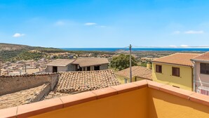 Blick von einem Balkon auf eine Küstenstadt mit Häusern mit Terrakotta-Dächern und blauem Himmel.