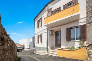 Un bâtiment à deux étages avec une façade jaune, des volets bruns et un petit porche à l’avant.