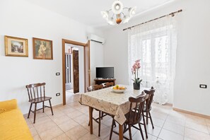 Un coin repas comprenant une table, des chaises, un téléviseur et une fenêtre avec des rideaux.