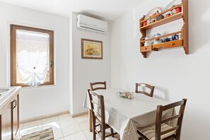 A dining area with a table, chairs, a window, an air conditioner, and a shelf with dishes.