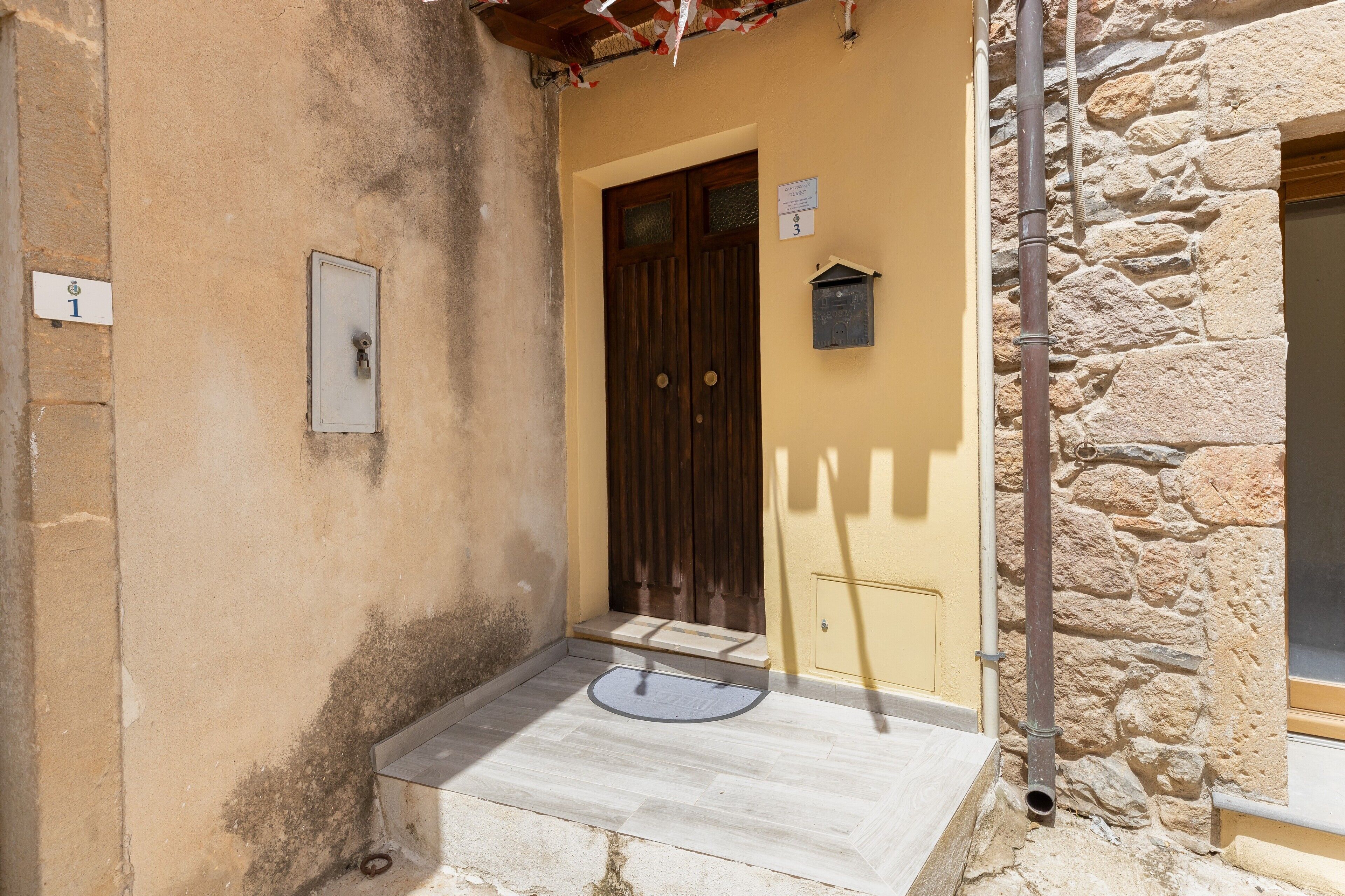 Une entrée d’immeuble avec une porte en bois, une boîte aux lettres et une plaque indiquant le numéro de l’immeble.