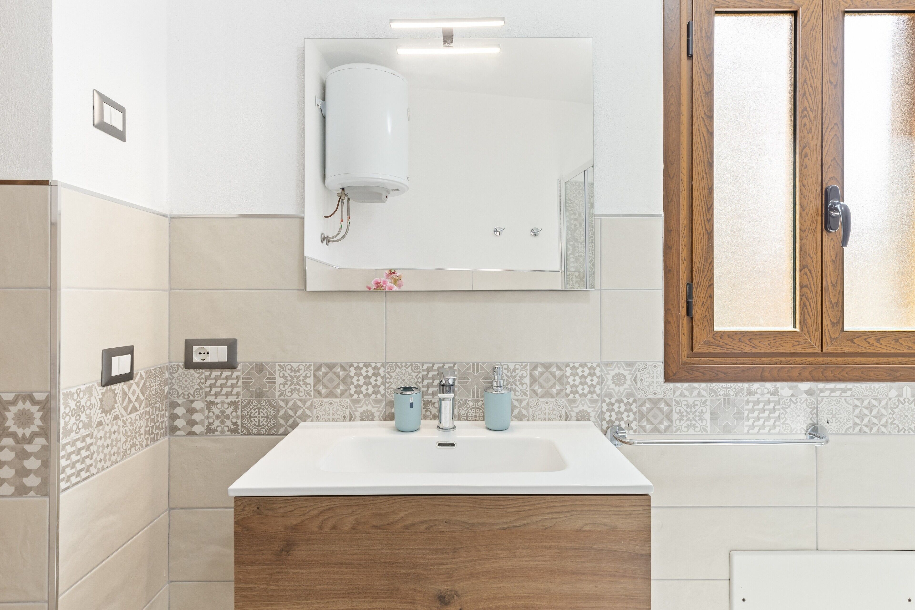 A bathroom with a white sink, wooden cabinet, patterned tiles, and a mirror above the sink.