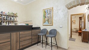 A bar area with stools, a shelf of bottles, and a framed painting on the wall. - Room 'Clio' with shared terrace, Wi-Fi and air conditioning (Scano di Montiferro)