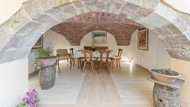 A dining area with a stone arch, wooden chairs, a table, and potted plants. - Room 'Clio' with shared terrace, Wi-Fi and air conditioning (Scano di Montiferro)