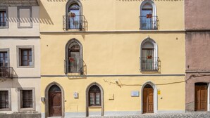 A multi-story building with arched windows and balconies, a cobblestone street, and a clear blue sky. - Room 'Clio' with shared terrace, Wi-Fi and air conditioning (Scano di Montiferro)