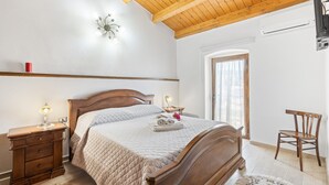 Ein Schlafzimmer mit einem hölzernen Bett, Nachttischen, einem kleinen Tisch, einem Stuhl, einem Fenster und einem Deckenventilator.