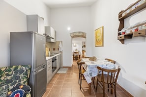 A compact kitchen with a refrigerator, oven, and sink. There is a dining table with chairs and a patterned tablecloth.