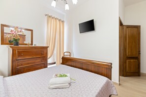 Un dormitorio con cama, cómoda, espejo, televisor y puerta de madera.