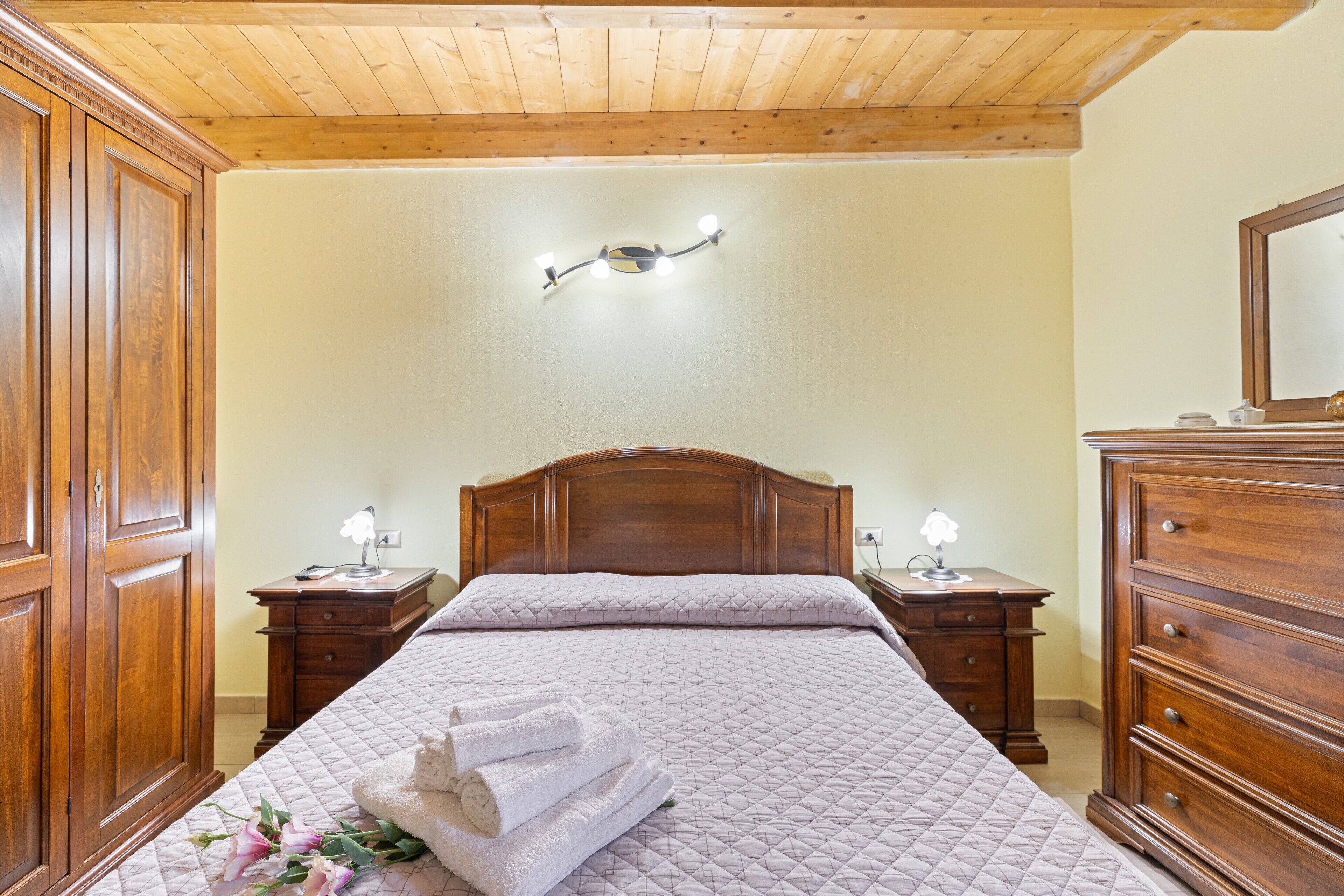 Ein Schlafzimmer mit Holzboden, einem Bett mit gesteppter Bettdecke, zwei Nachttischen mit Lampen, einem Holzschrank und einer Wandleuchte.