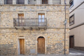 Un edificio de piedra con dos puertas de madera, un balcón con barandilla de metal y una ventana pequeña.