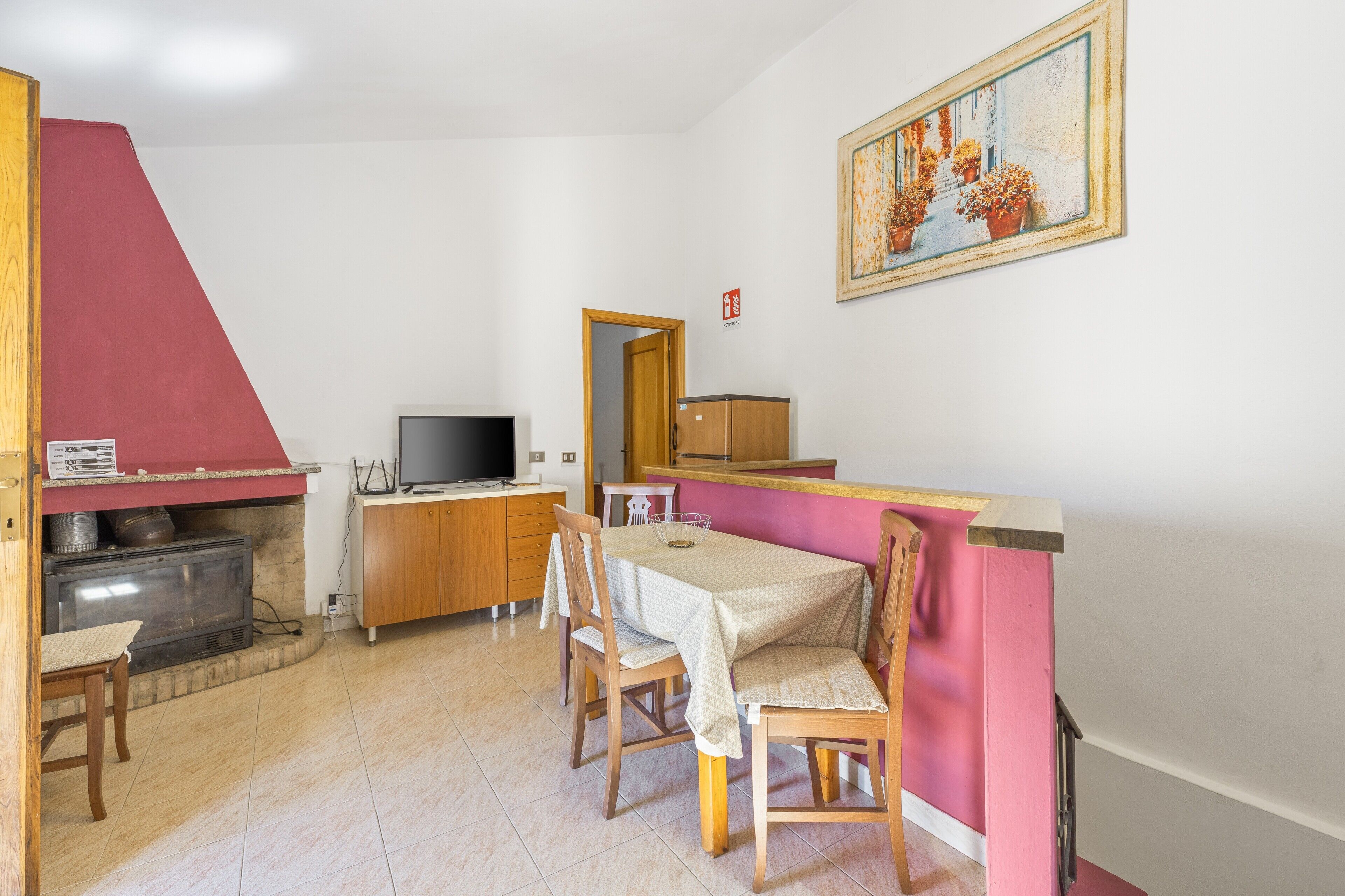 Un comedor con mesa, sillas, televisor y una zona de cocina con armarios y pared roja.