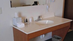 A bathroom with a white sink, a mirror, a towel dispenser, and a trash bin. - Guardian Inn (Le Center)