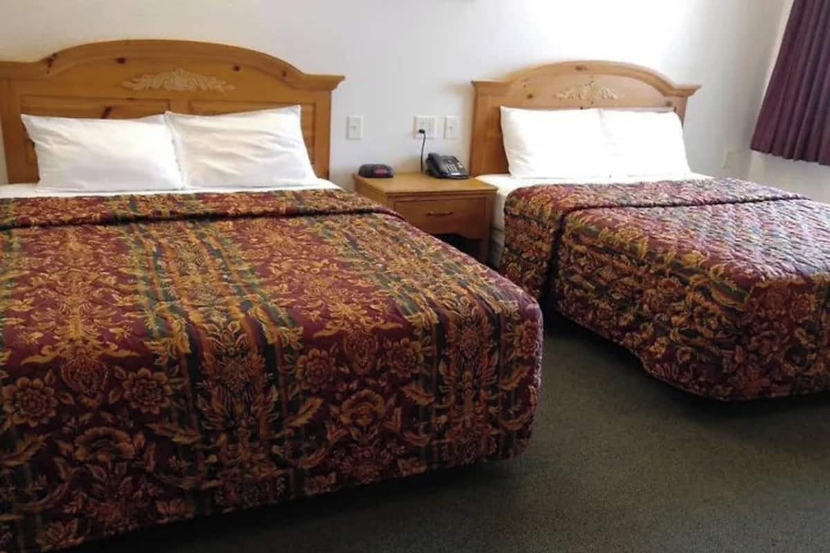 Two double beds with floral-patterned bedding, wooden headboards, and a bedside table with a telephone.