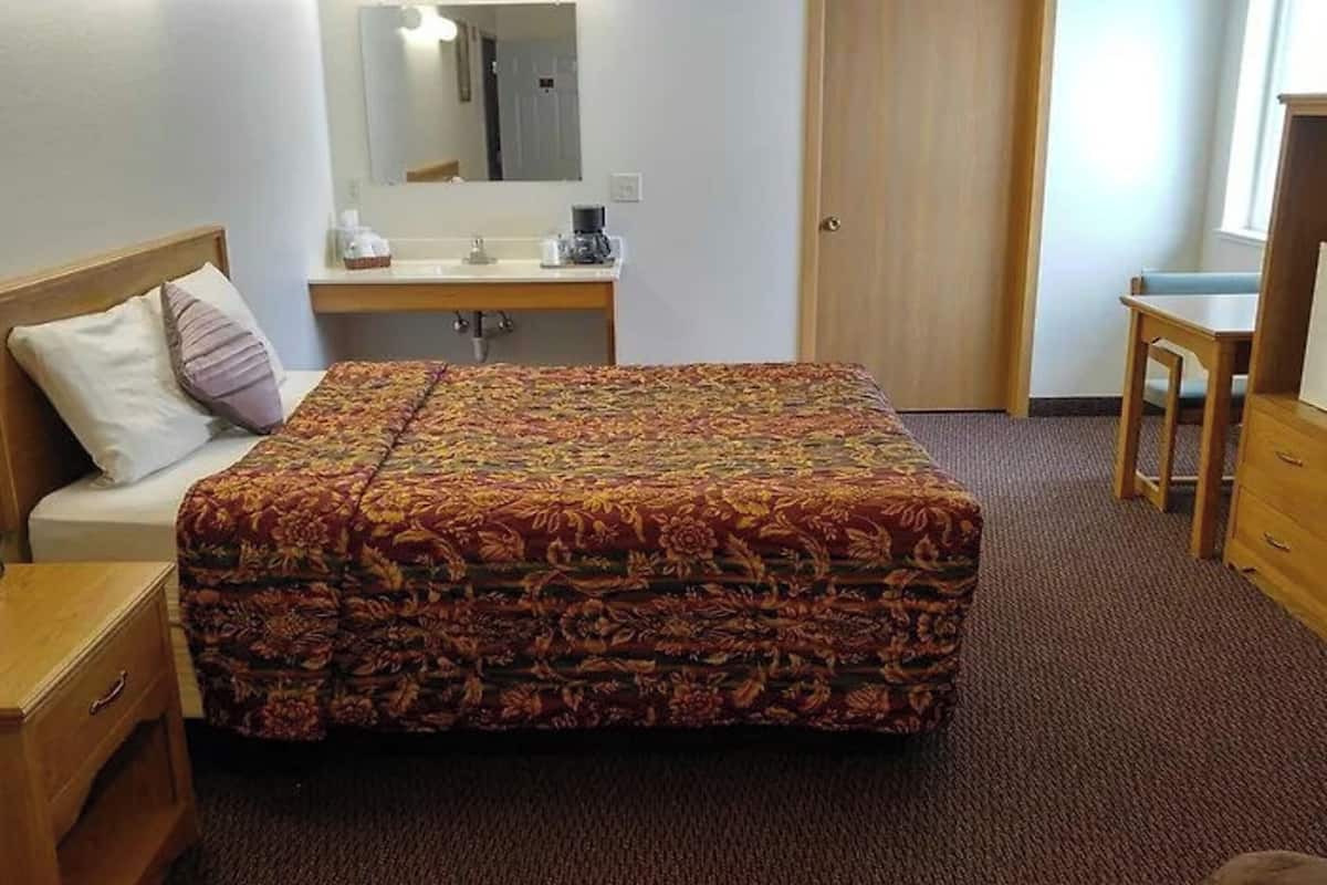 A hotel room with a bed, a desk, a chair, a dresser, a mirror, and a door.