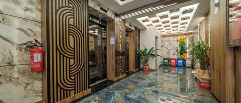 A modern lobby with marble flooring, wooden paneling, and a ceiling with geometric light fixtures.