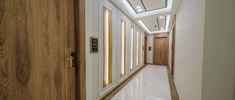 Un pasillo con puertas de madera, luces verticales iluminadas y un suelo de mármol pulido.