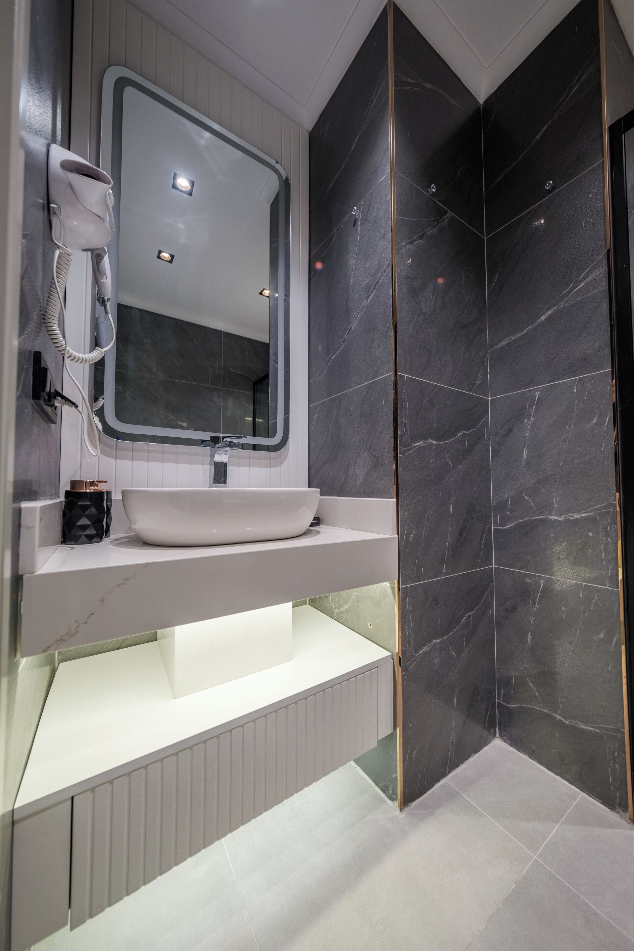 A modern bathroom with a white vanity, a large mirror, and a black marble shower enclosure.