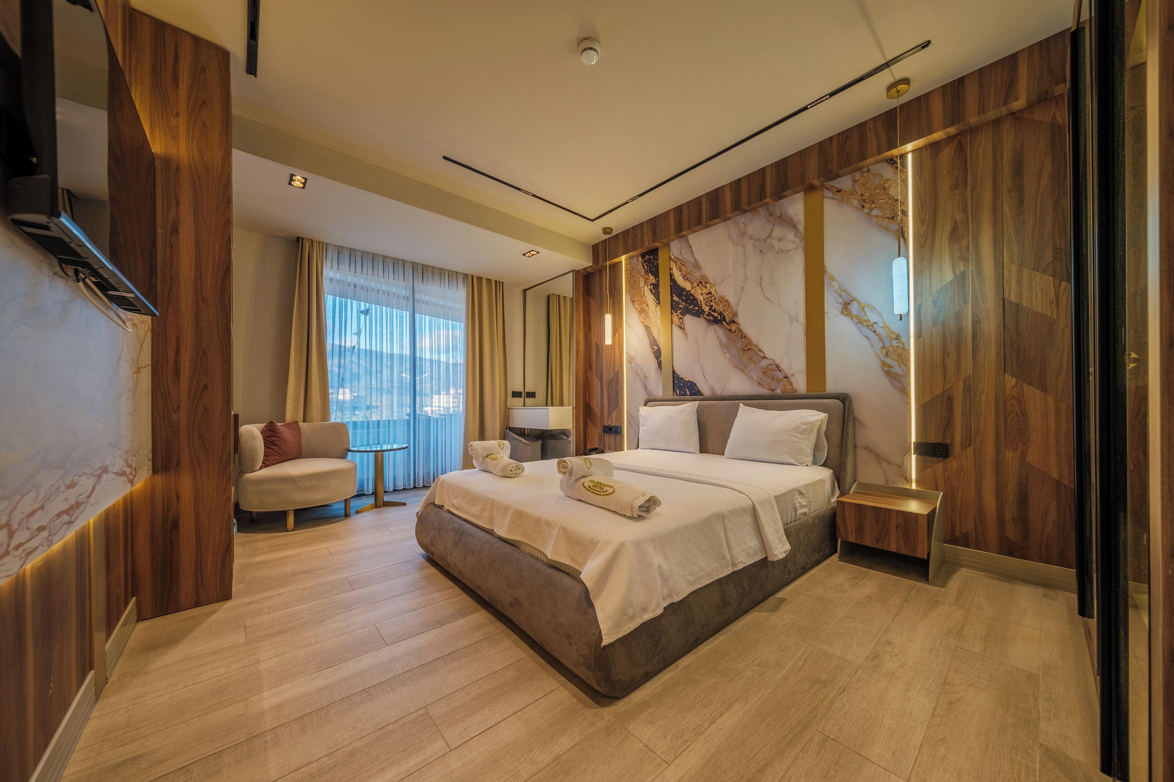 A modern hotel room with a large bed, a sofa, a nightstand, and a marble accent wall.