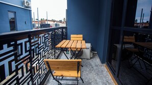 A balcony with wooden tables and chairs, a patterned metal railing, and a view of the cityscape.