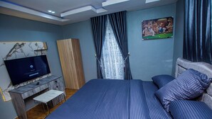 A bedroom with a bed, a TV, a wooden wardrobe, and a painting on the wall.