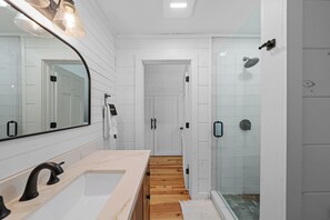 A modern bathroom with a large mirror, a sink, and a shower area.