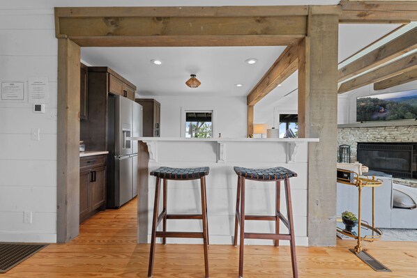 A modern kitchen with wooden beams, stainless steel appliances, and a large TV screen.