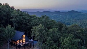 A cabin with a deck, surrounded by dense forest and mountains in the background. - Panoramic Views! Wrap around Deck, Hot Tub & Grill (Morganton)