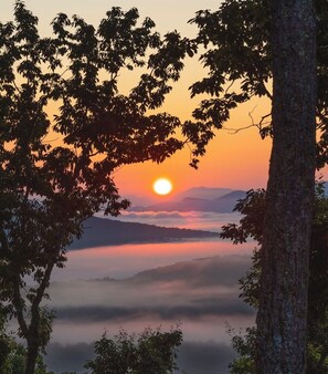 A sunrise over a mountainous landscape with trees in the foreground.