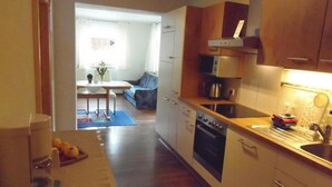Cocina compacta con estufa, microondas y pileta. Se observa en el fondo un comedor con mesa y sillas.