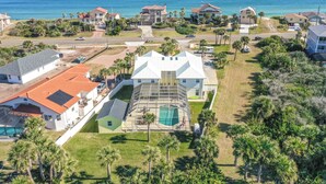 Vue aérienne d’un quartier résidentiel situé sur la côte, avec des maisons, une piscine et un grand bâtiment blanc doté d’un toit végétalisé.