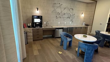 Eine moderne Küche mit Backofen, einer Kaffeemaschine und einem Essbereich mit blauen Stühlen und einem runden Tisch.