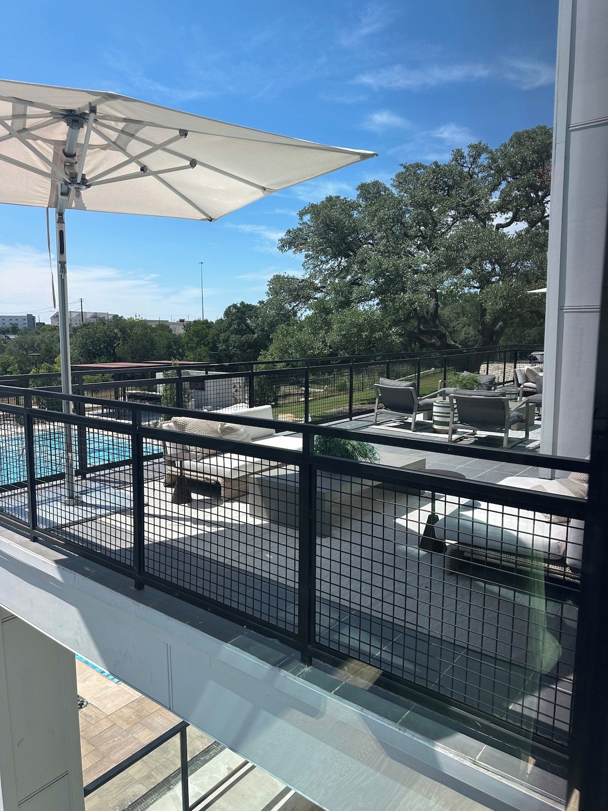A rooftop pool area with a fenced enclosure, outdoor seating, and a large umbrella.
