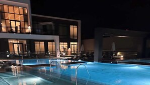En swimmingpool med fliseterrasse og en moderne bygning i baggrunden.