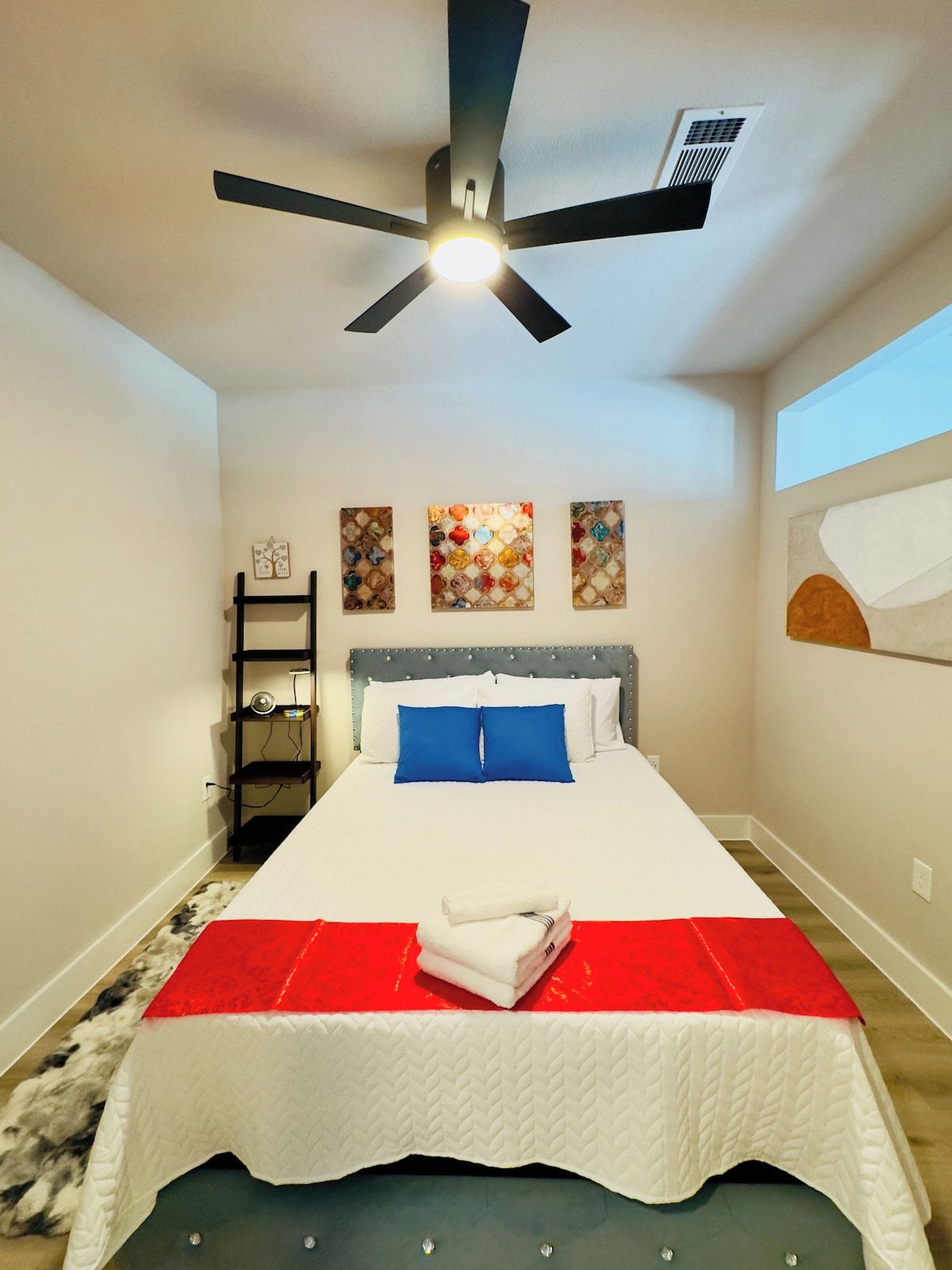 Un dormitorio con una cama, un ventilador de techo, un estante en la pared y obras de arte.