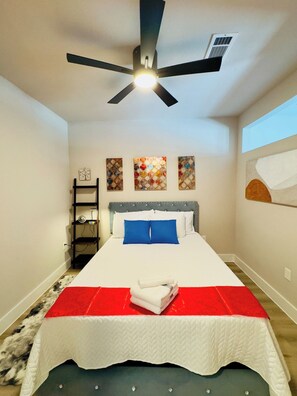 Un dormitorio con una cama, un ventilador de techo, un estante en la pared y obras de arte.