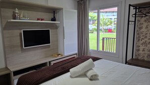 Ein Hotelzimmer mit Bett, einem an einer Holzwand montierten Fernseher, einem Balkon mit Blick auf Grünflächen und einem hängenden Kleiderhaken.
