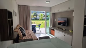 Ein modernes Hotelzimmer mit Bett, Fernseher, Balkon mit Tisch und Stühlen und Blick auf eine grüne Landschaft.