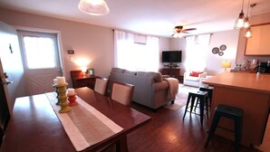 Een gezellige woonkamer met een bank, een televisie en een eethoek met een tafel en stoelen.
