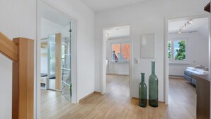 Et rummeligt værelse med trægulv, en glasdør til en balkon og udsigt til en murstensbygning.