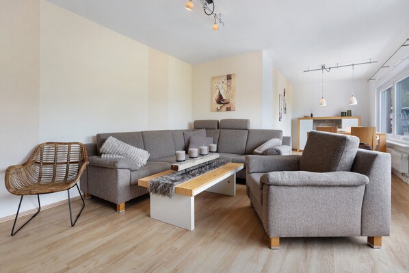 Un salon moderne avec un canapé gris, une table basse en bois et un fauteuil en osier.