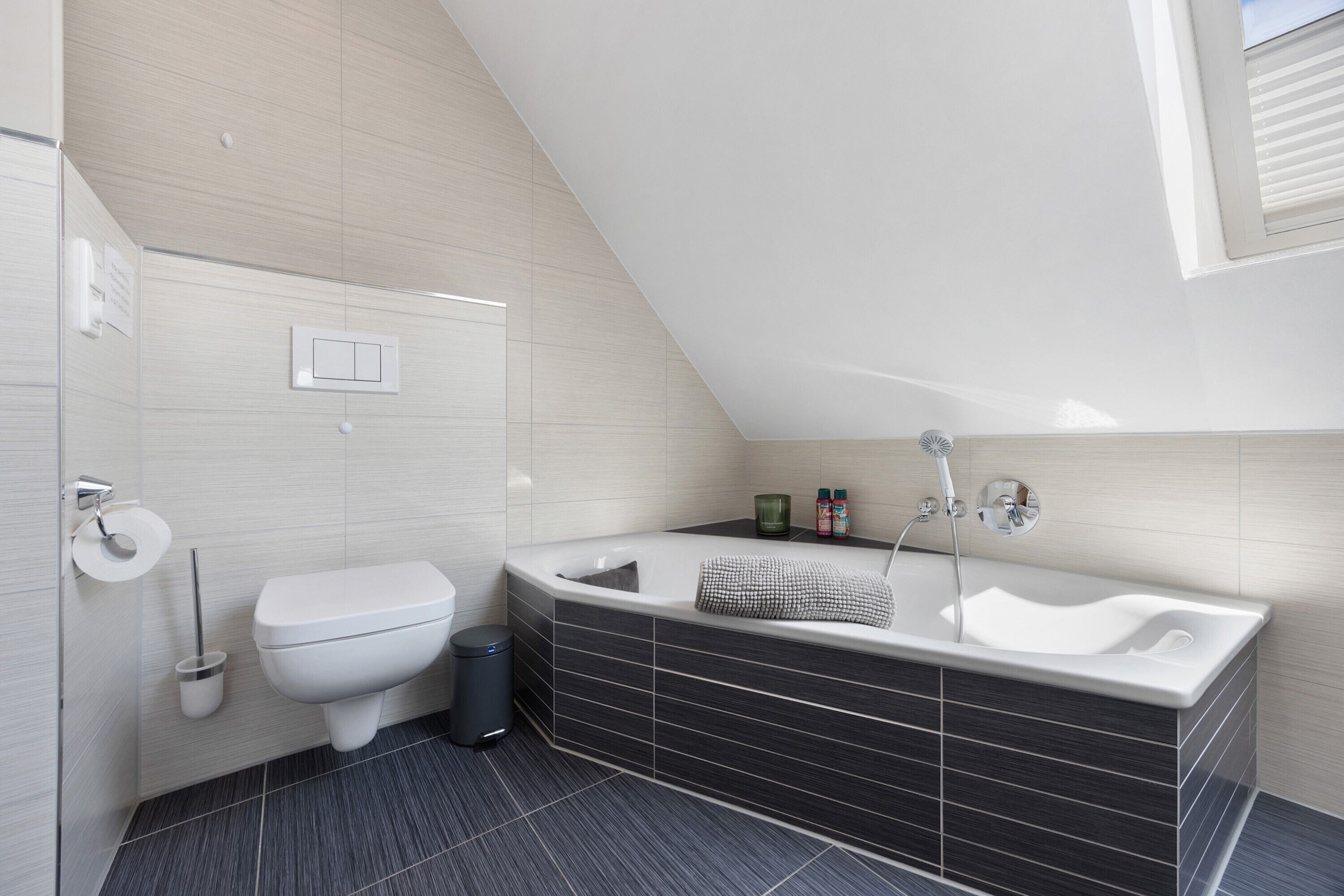 Een moderne badkamer met een badkuip, toilet en een raam.