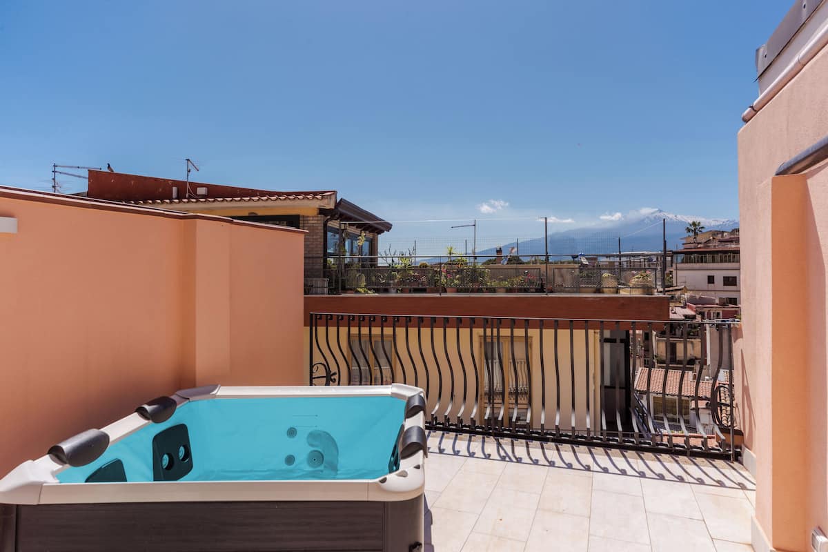Eine Dachterrasse mit Whirlpool, Blick auf ein Gebirge und ein Balkon mit Geländer.