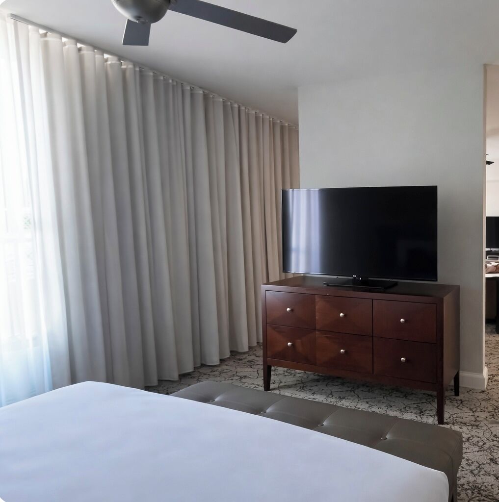 A hotel room with a bed, a TV on a wooden dresser, and a ceiling fan.