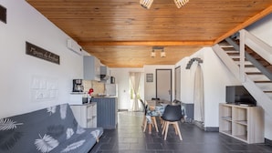 Een moderne leefruimte met een houten plafond, een eethoek met tafel en stoelen, een bank met bladprint, een keuken en een trap.