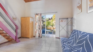 Une pièce avec un escalier en bois, un canapé bleu, un meuble en bois et une vue sur l’extérieur grâce à une porte vitrée.