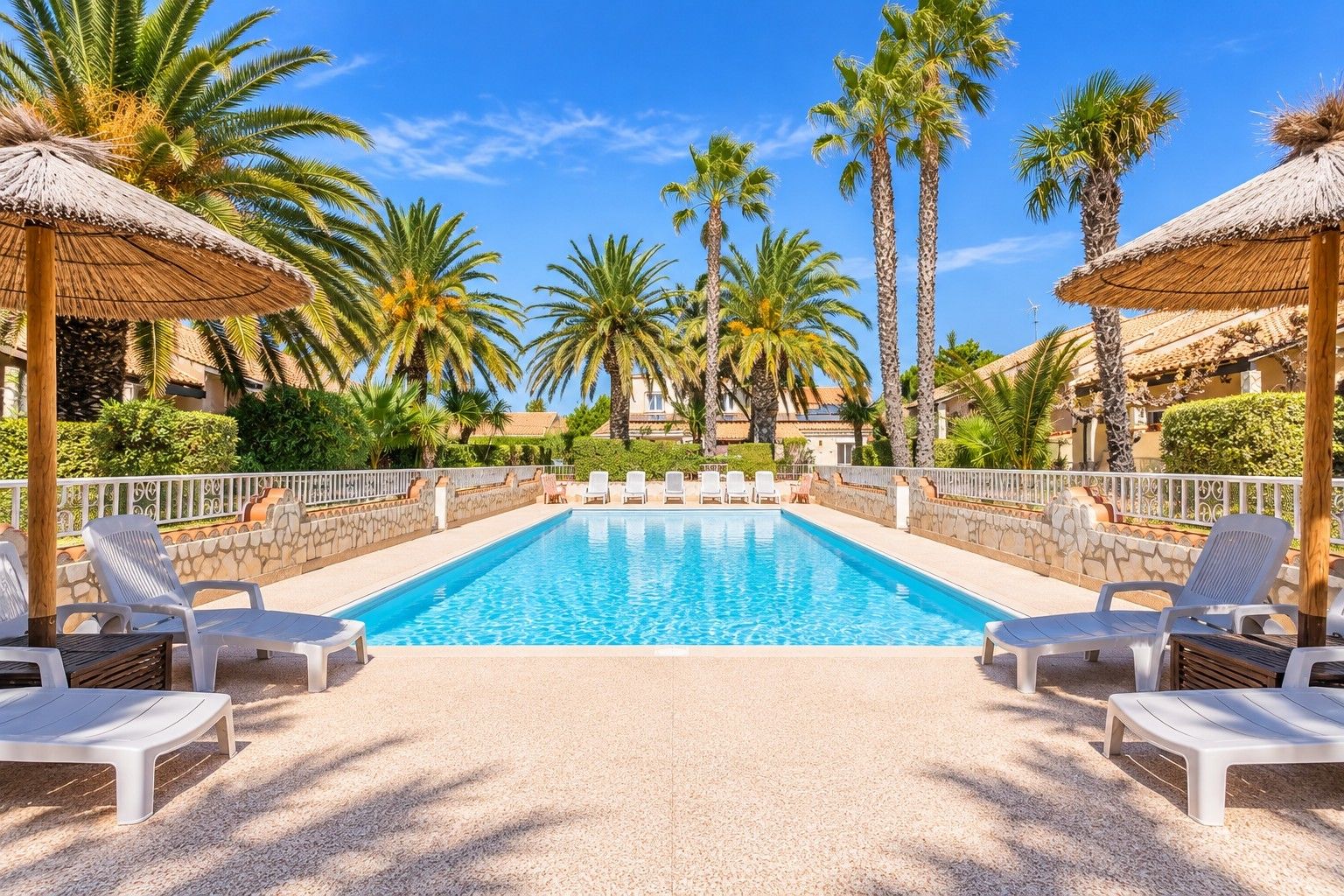 A swimming pool with lounge chairs and palm trees.