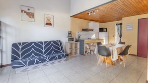 Un espace de vie compact comprenant un canapé, une table à manger, des chaises, un coin cuisine et une porte rouge.