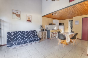 Espai vital compacte amb sofà, taula de menjador, cadires, petita cuina i una porta vermella.