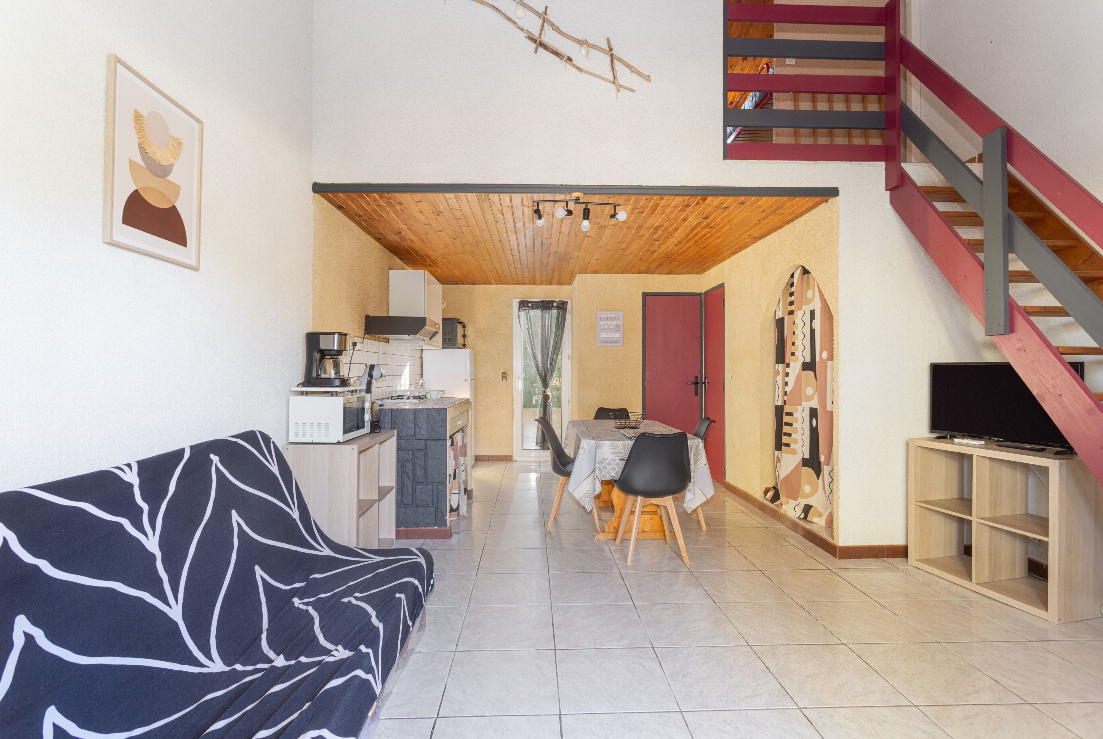 Una sala de estar con un sofá, un comedor con mesa y sillas, una cocina equipada y una escalera.